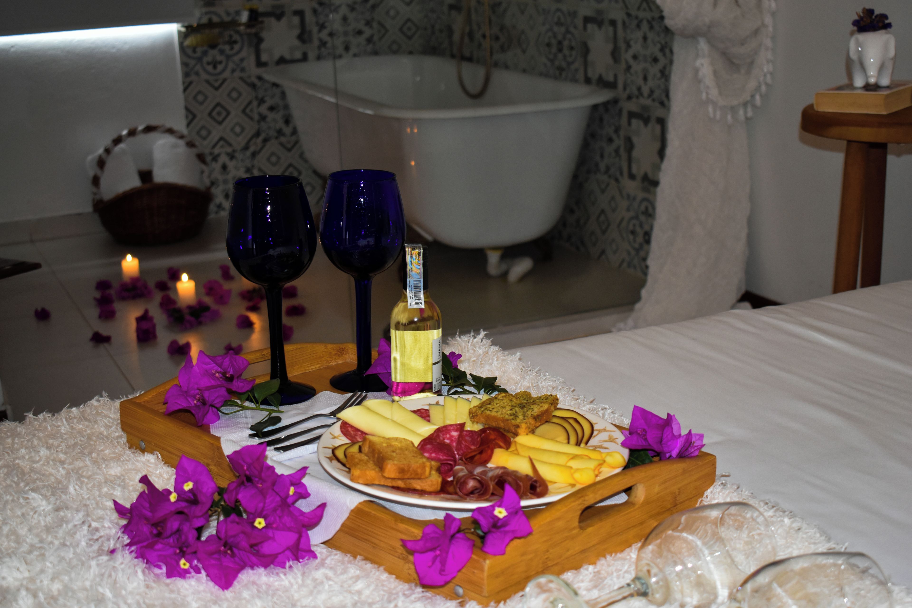 A tray with food and drinks, a bathtub, and a white bed in the background.