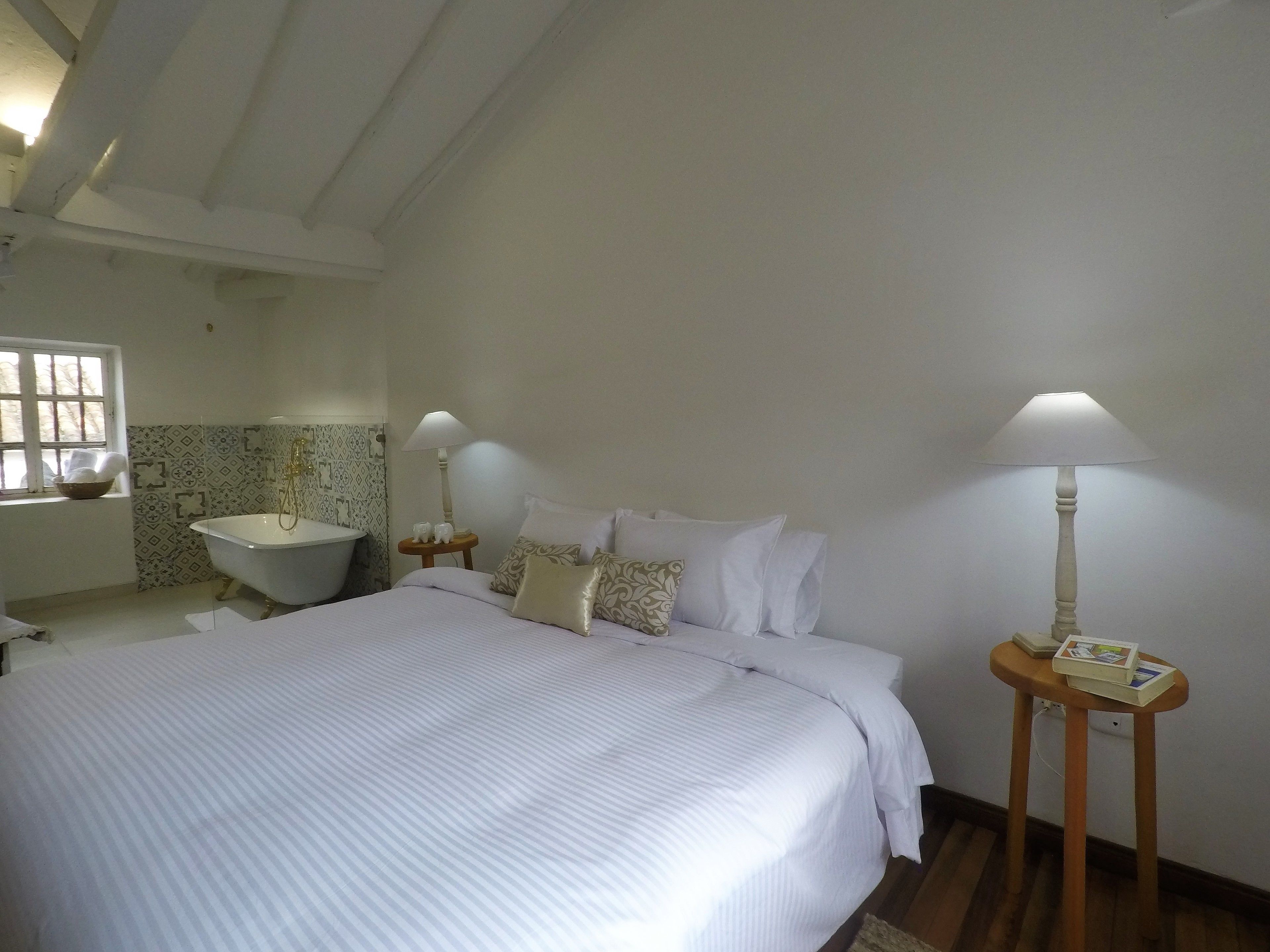 A bedroom with a large bed, two bedside tables with lamps, a window, and a bathroom with a bathtub.