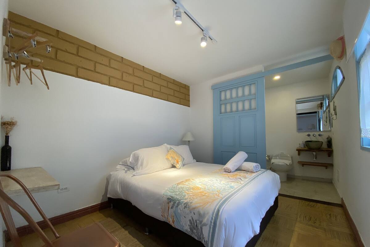 A bedroom with a bed, a chair, a nightstand, a dresser, a mirror, and a bathroom with a sink and toilet.