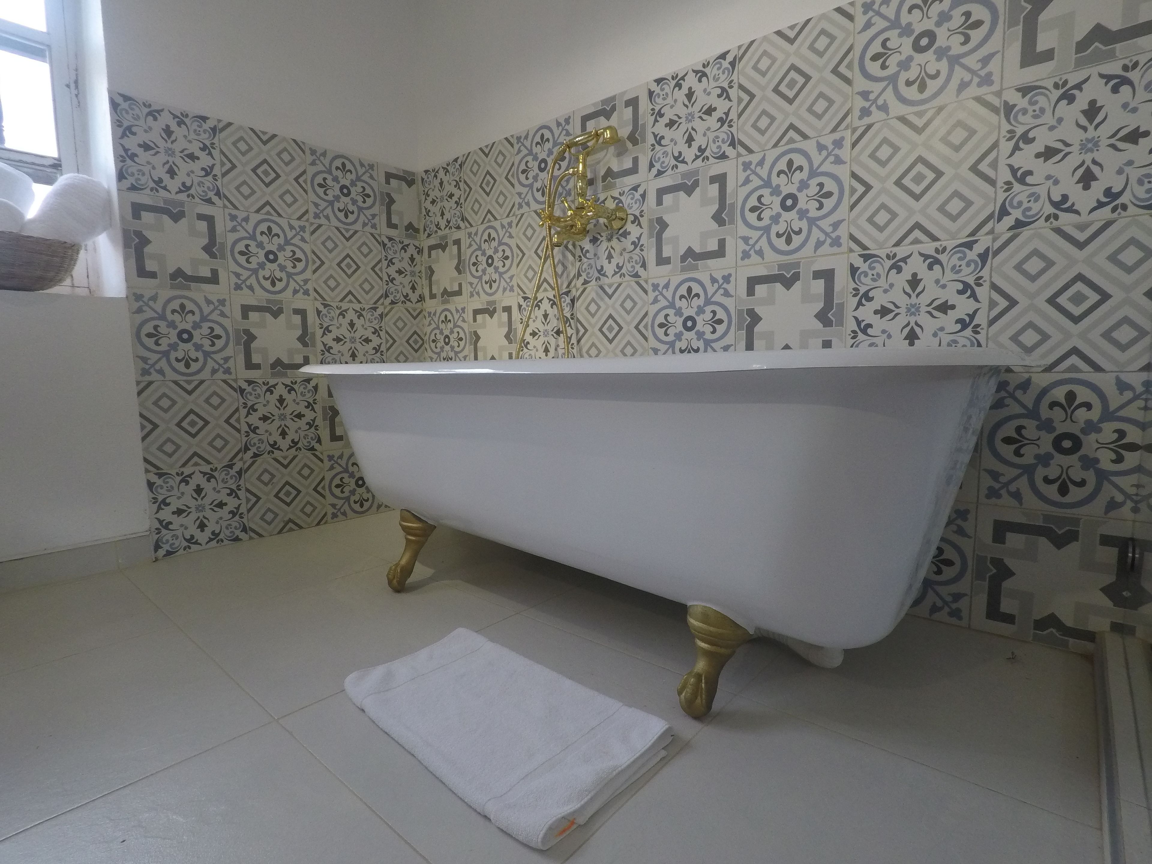 Ein Badezimmer mit einer freistehenden Badewanne, gemusterten Fliesen an den Wänden und einem weißen Handtuch auf dem Boden.