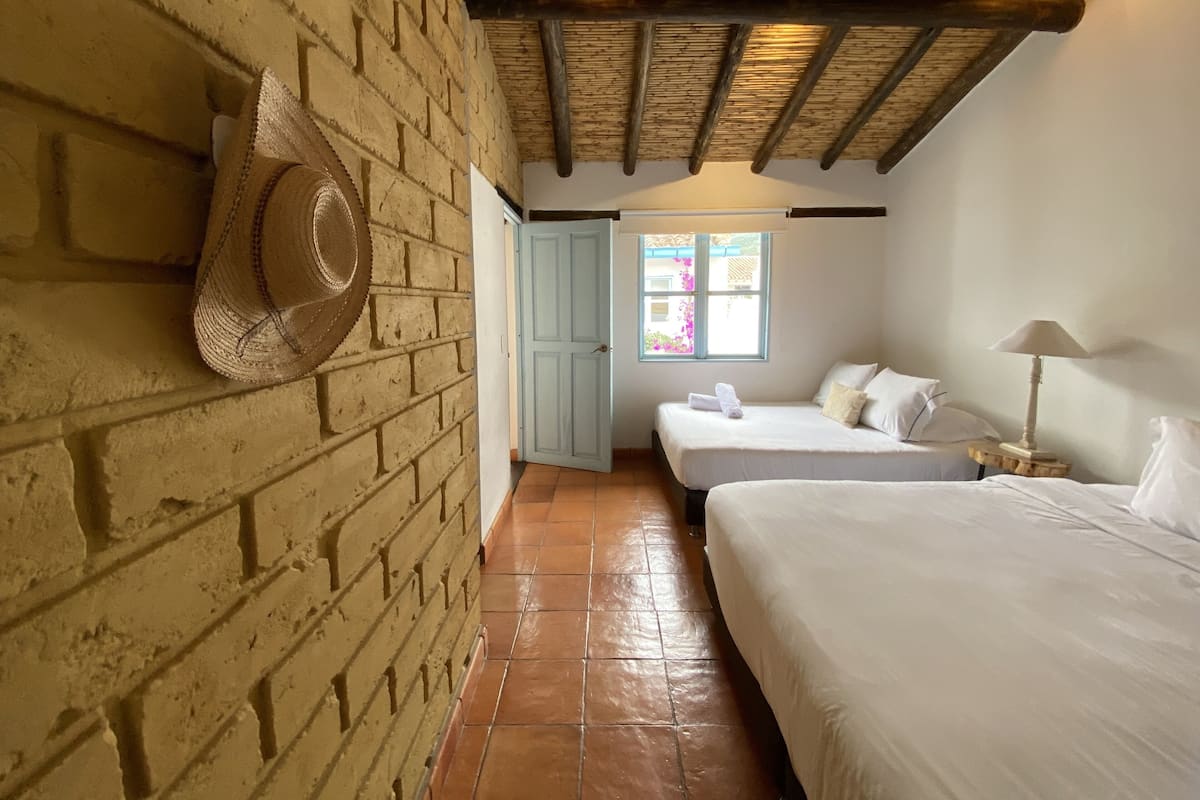 A room with a brick wall, a wooden ceiling, a window with a view, and two beds.