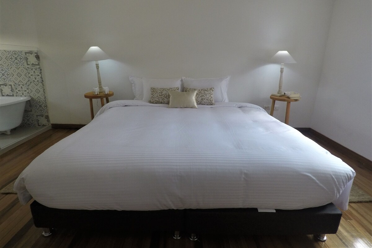 Una cama bien hecha con sábanas blancas, dos lámparas de noche y un papel tapiz estampado.