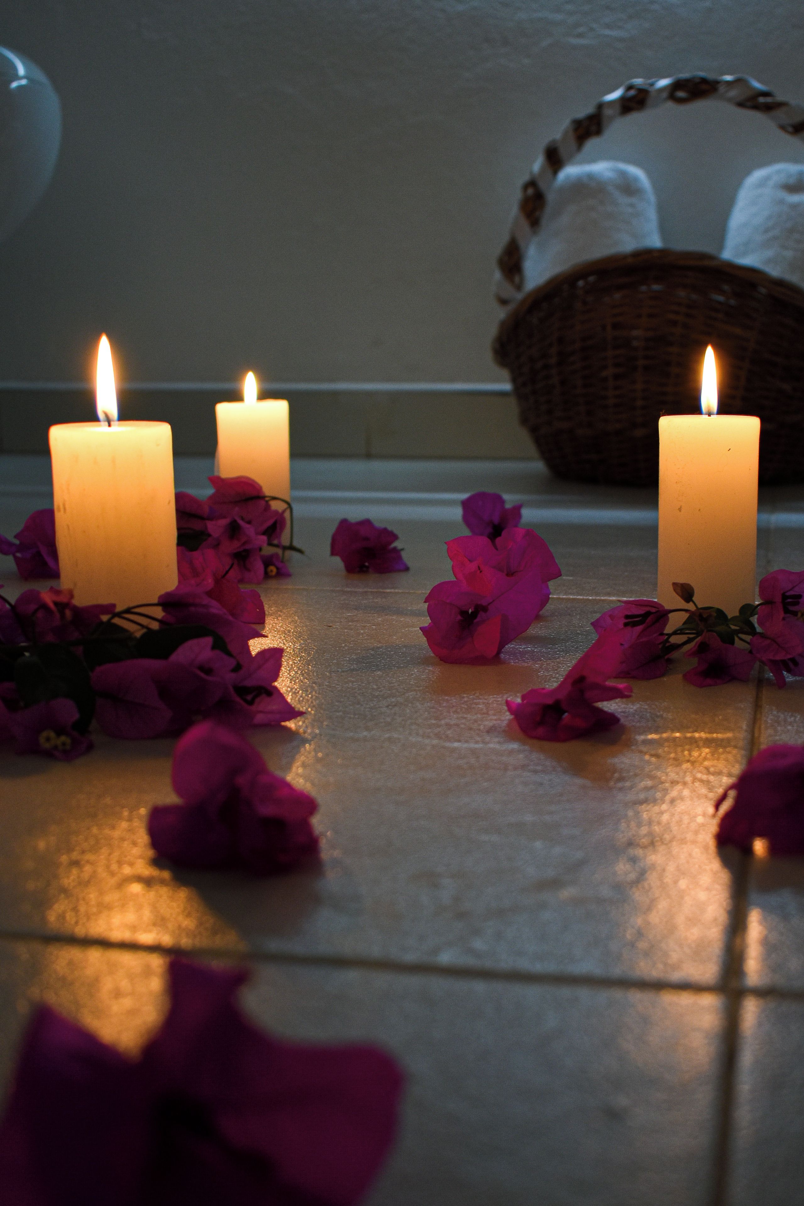 Three lit candles on a tiled floor with scattered rose petals.