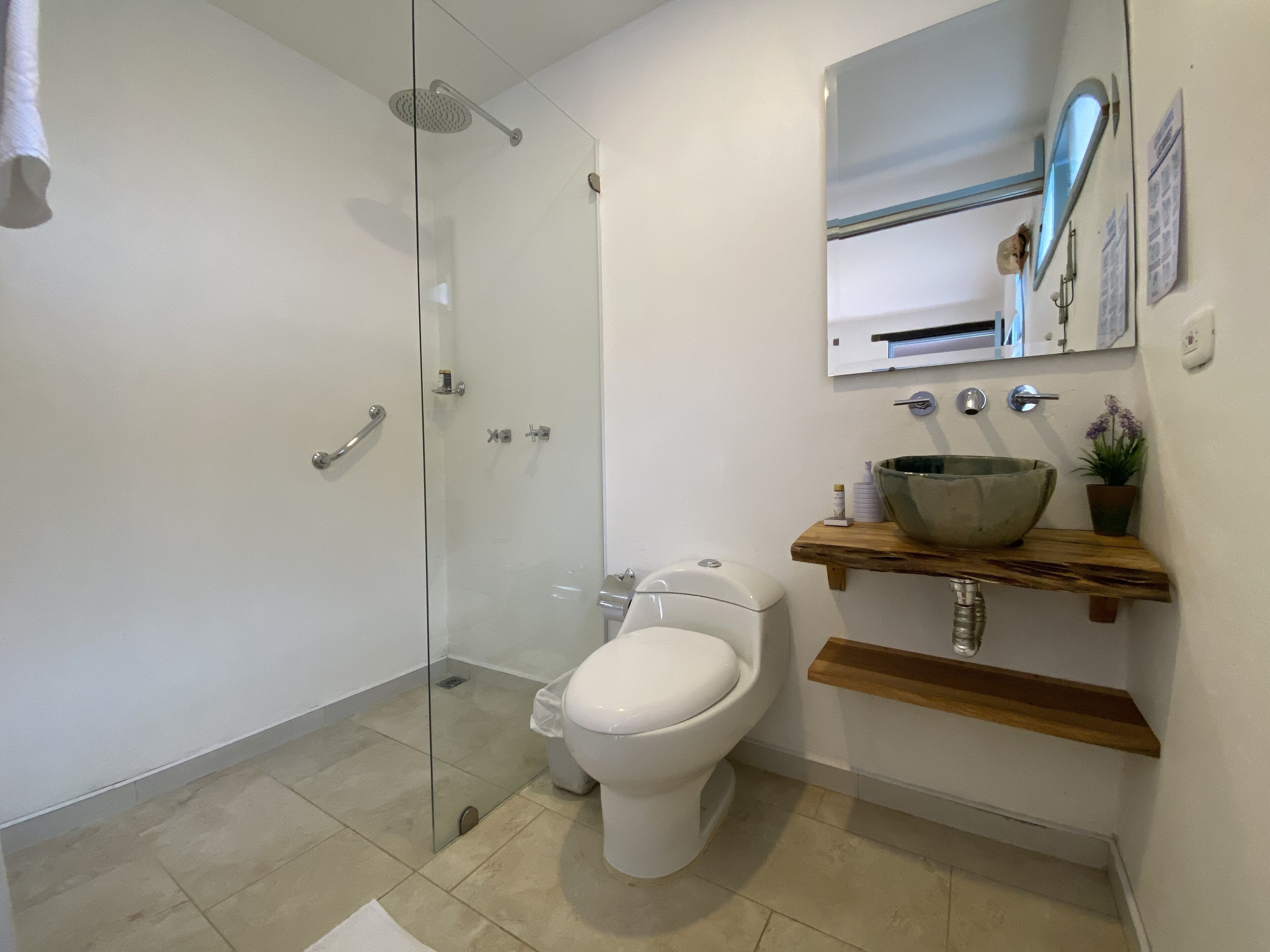 A modern bathroom with a glass-enclosed shower, a white toilet, and a wooden vanity with a large bowl sink.