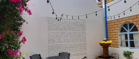 An outdoor patio with a table and chairs, a decorative fountain, and a wall with text.
