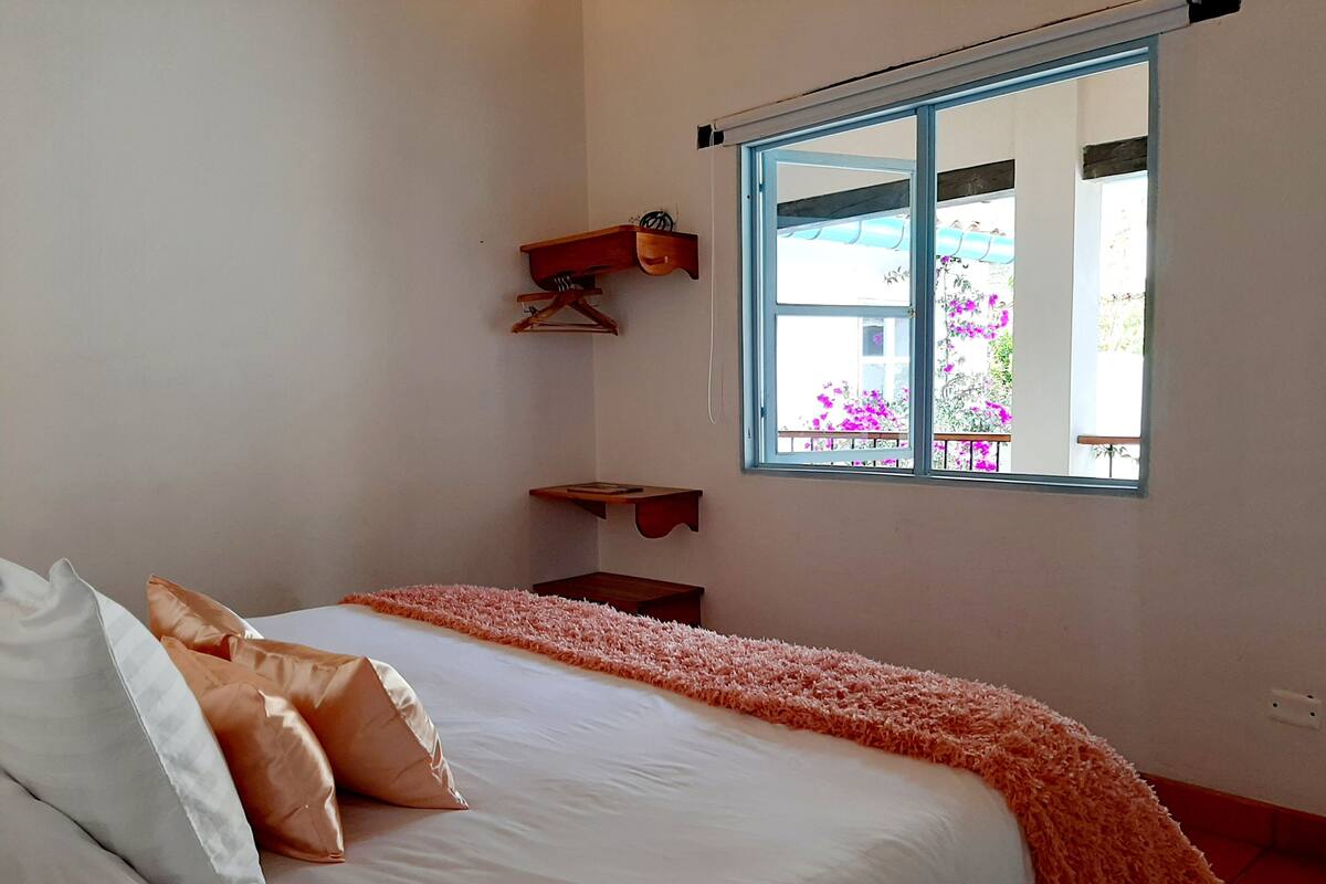 A bedroom with a bed, pillows, a window, and a view of flowers outside.