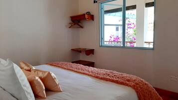 Un dormitorio con cama, almohadas, una ventana y vistas a flores afuera.