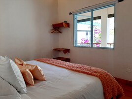 Un dormitorio con cama, almohadas, una ventana y vistas a flores afuera.