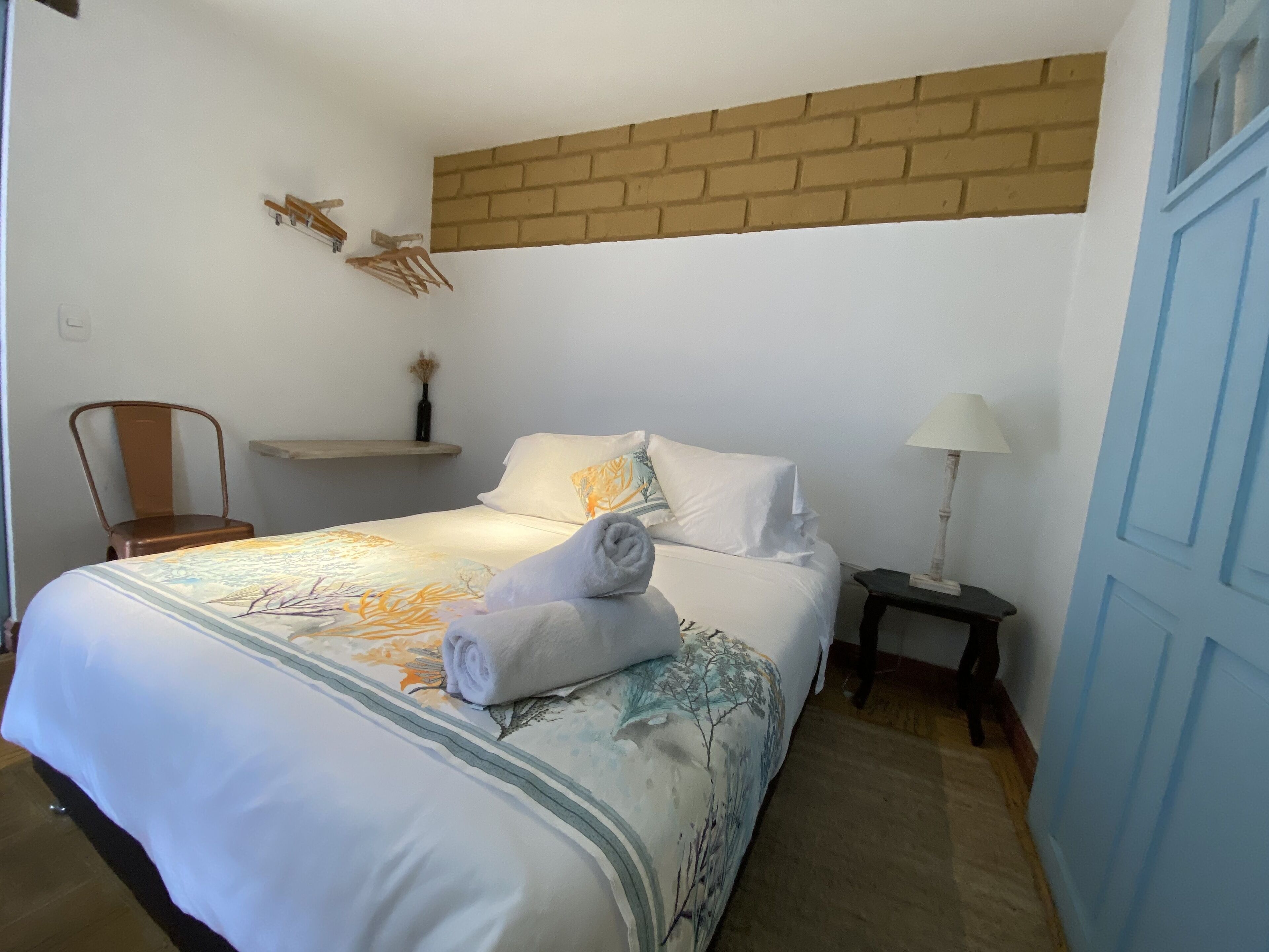 Un dormitorio con una cama, una silla, una mesita de noche, una lámpara y una pared de ladrillo decorativa.