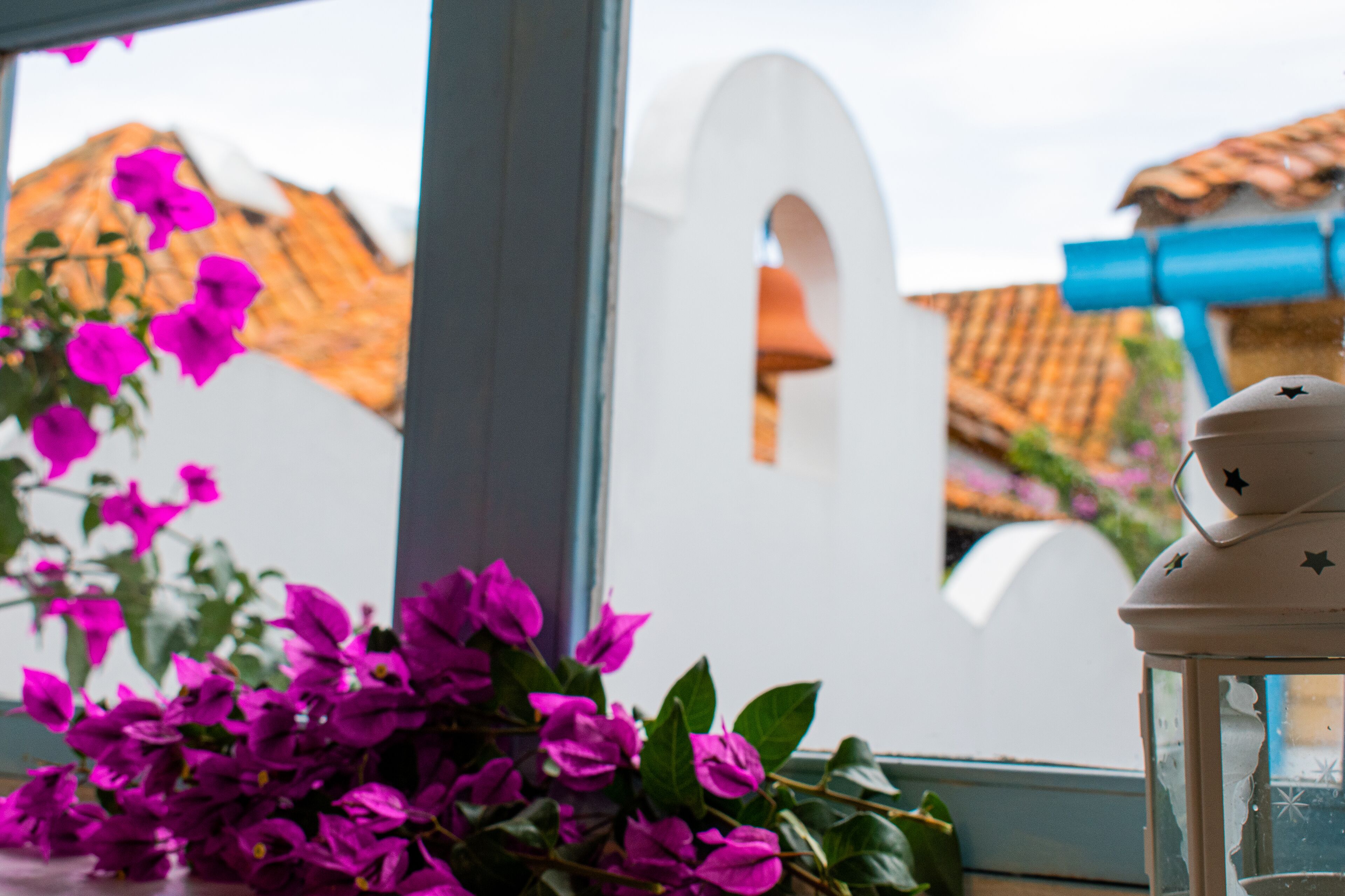 A window with a view of a building, a white archway, and a blue lantern.