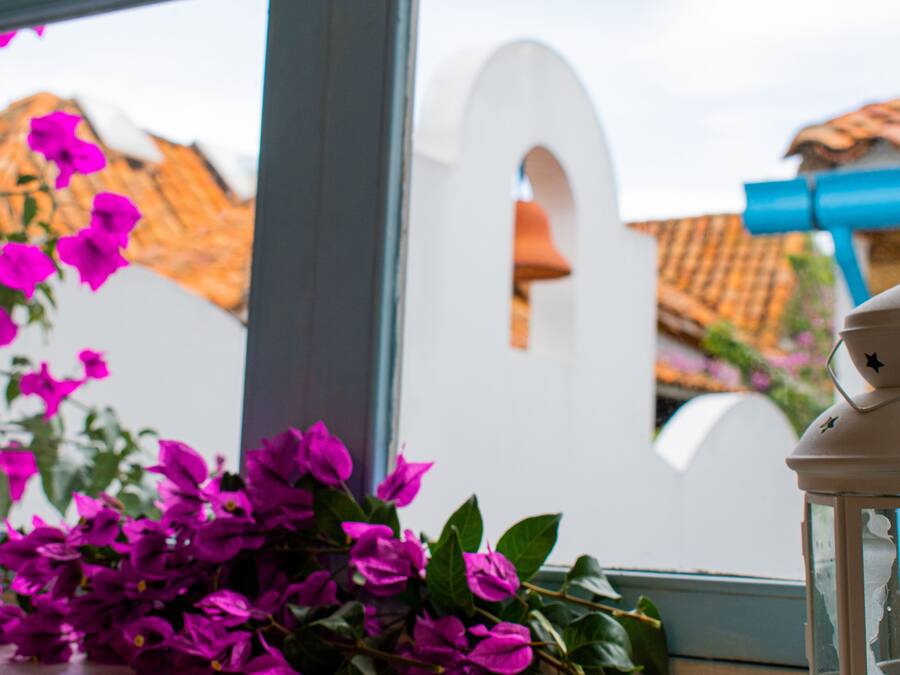 A window with a view of a building, a white archway, and a blue lantern.