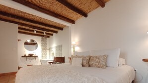 A bedroom with a large bed, a wooden ceiling, a bathroom with a mirror, and patterned tiles. - Casa Boutique Villa de Leyva - Adults only (Villa de Leyva)