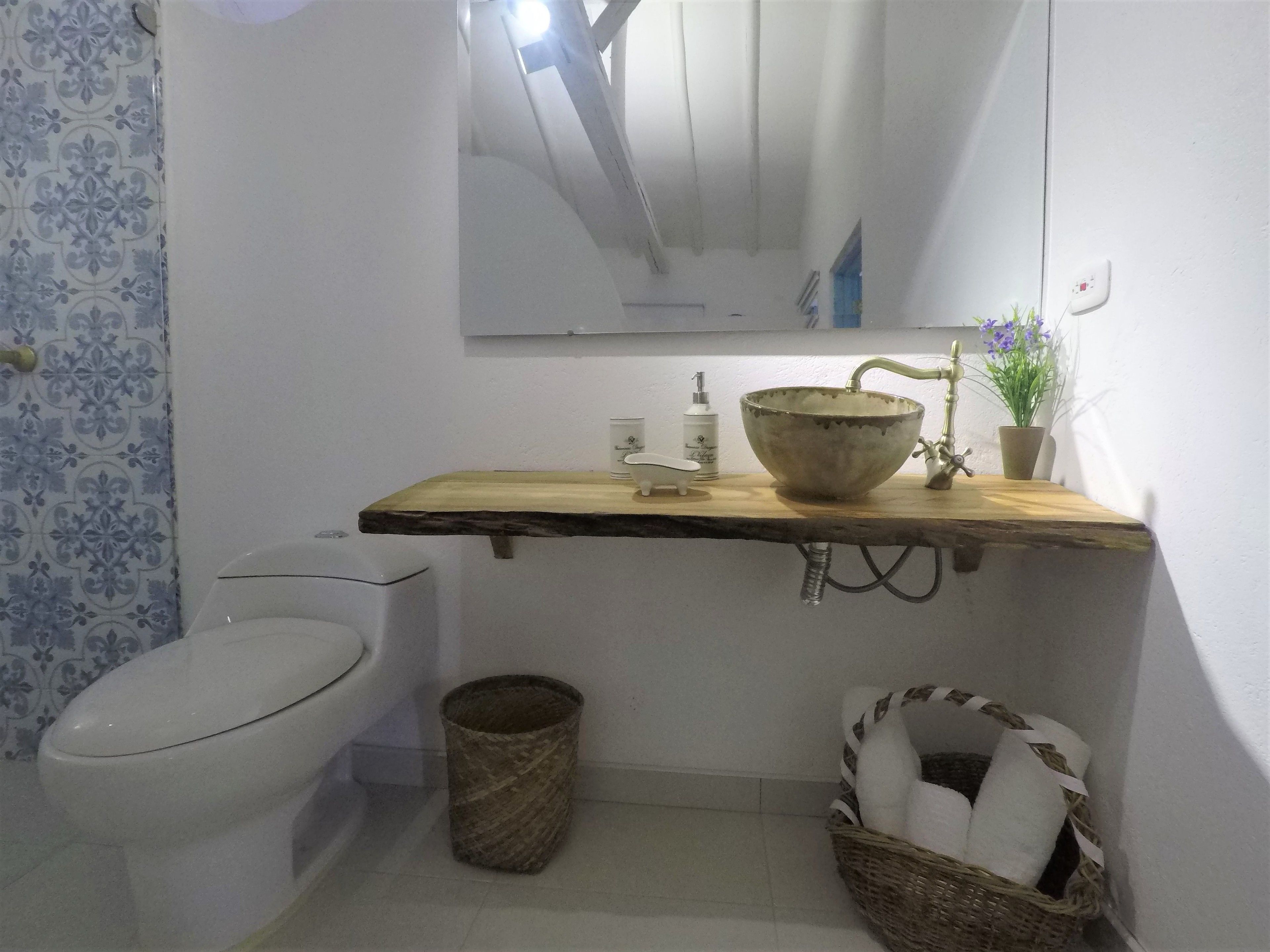 Ein Badezimmer mit Toilette, einem Waschbecken mit Holztischplatte, einem Spiegel, einer Topfpflanze und einem Mülleimer.