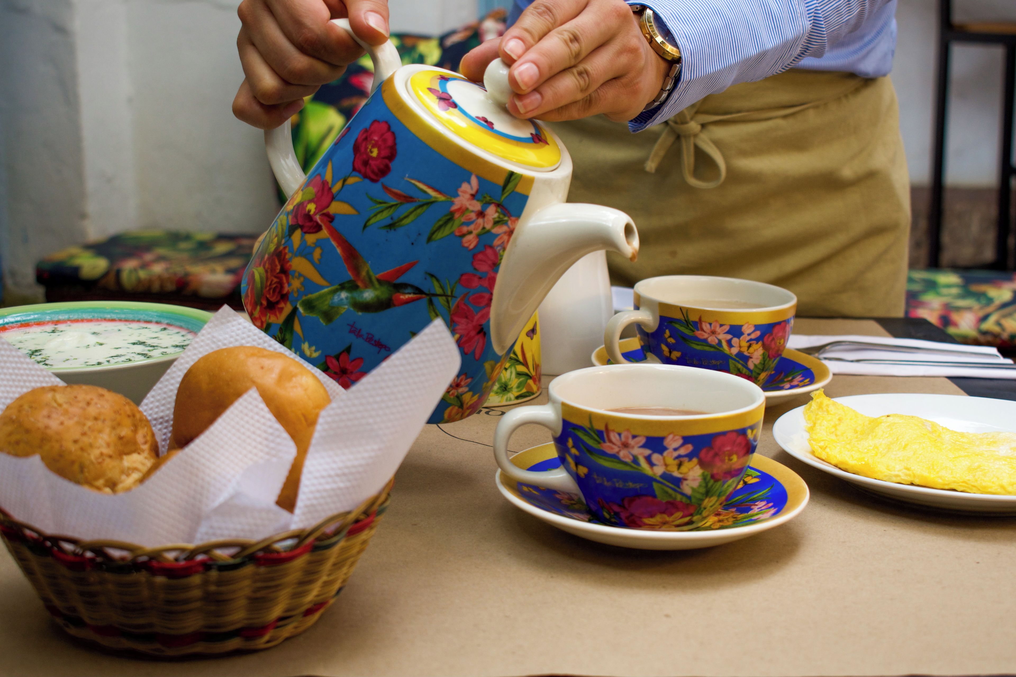 A table with a teapot, cups, a basket with bread, and an omelette.