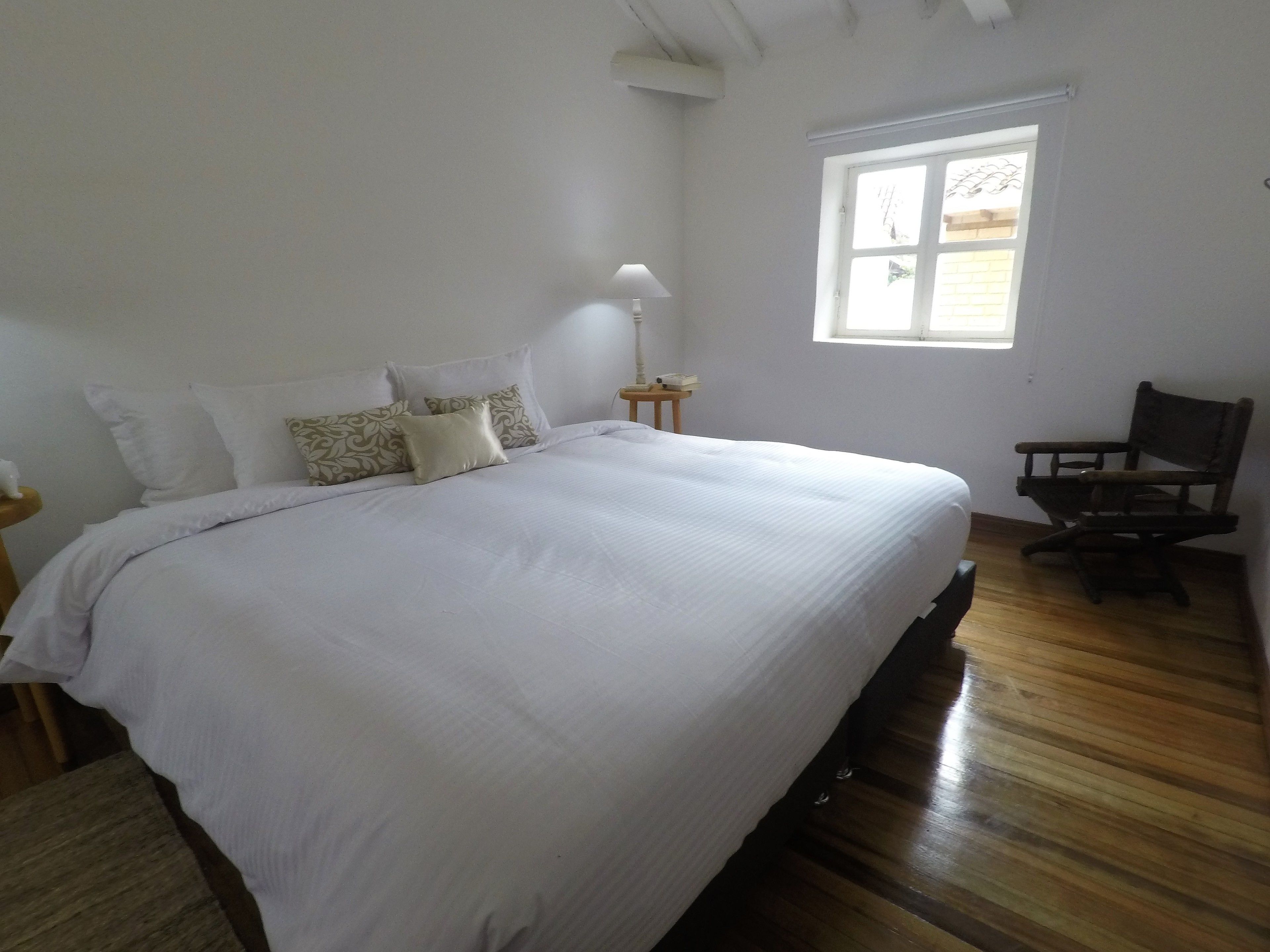 Un dormitorio con una cama grande, piso de madera, una ventana y una silla.