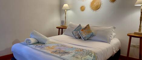 A neatly made bed with a floral bedspread, two pillows, and a rolled towel. There are two bedside tables with lamps, and wall art above the bed.