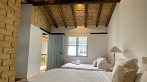 A room with two beds, a wooden ceiling, a brick wall, and a window with a view. - Casa Boutique Villa de Leyva - Adults only (Villa de Leyva)