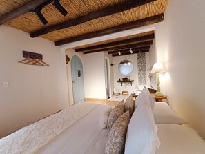 Un dormitorio con cama, techo de madera, baño con lavamanos y espejo, y una lámpara fijada a la pared.
