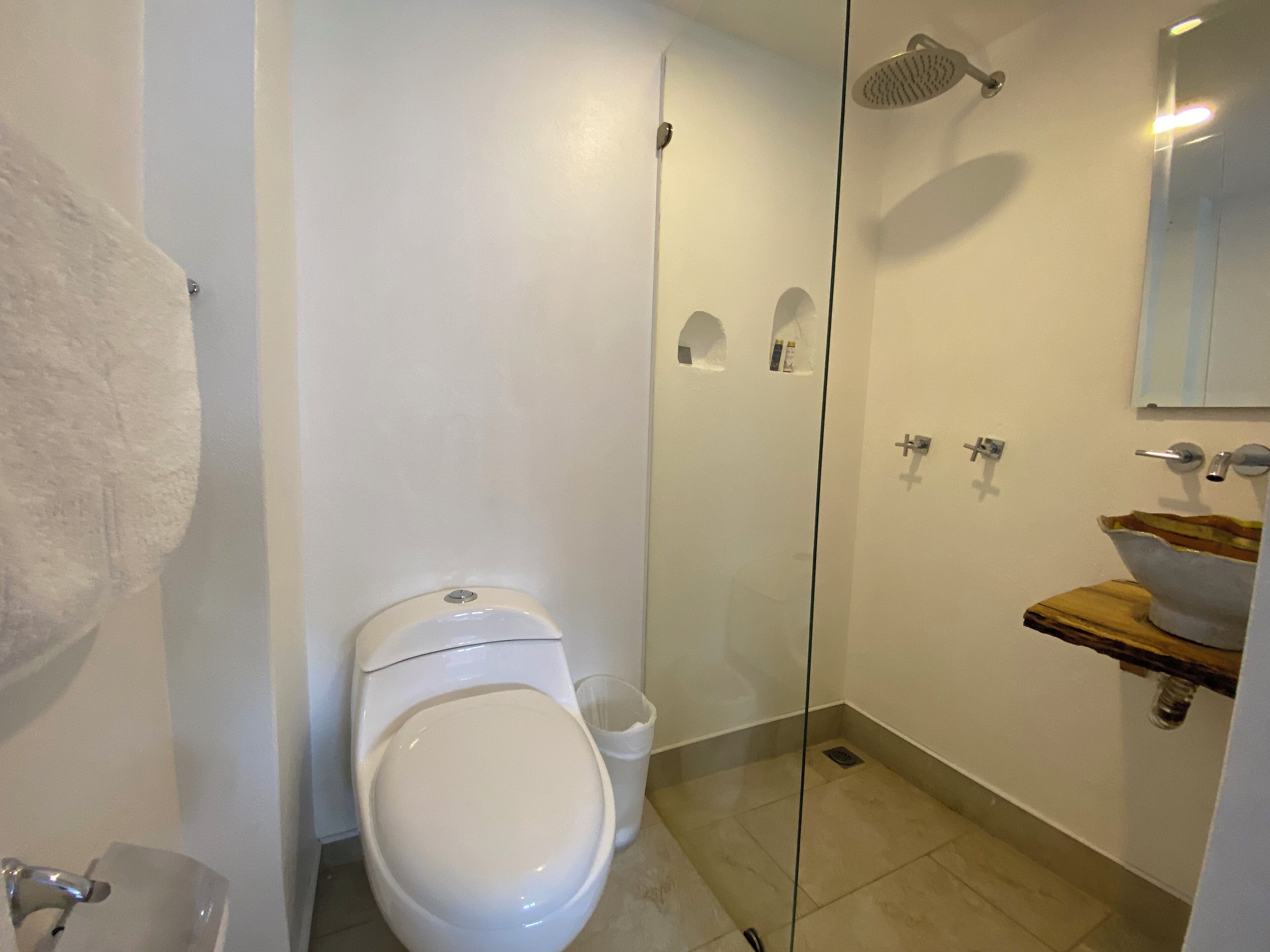 Un baño moderno con inodoro, cabina de ducha de vidrio, lavamanos con encimera de madera y barra para toallas.