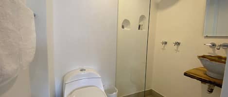 Un baño moderno con inodoro, cabina de ducha de vidrio, lavamanos con encimera de madera y barra para toallas.