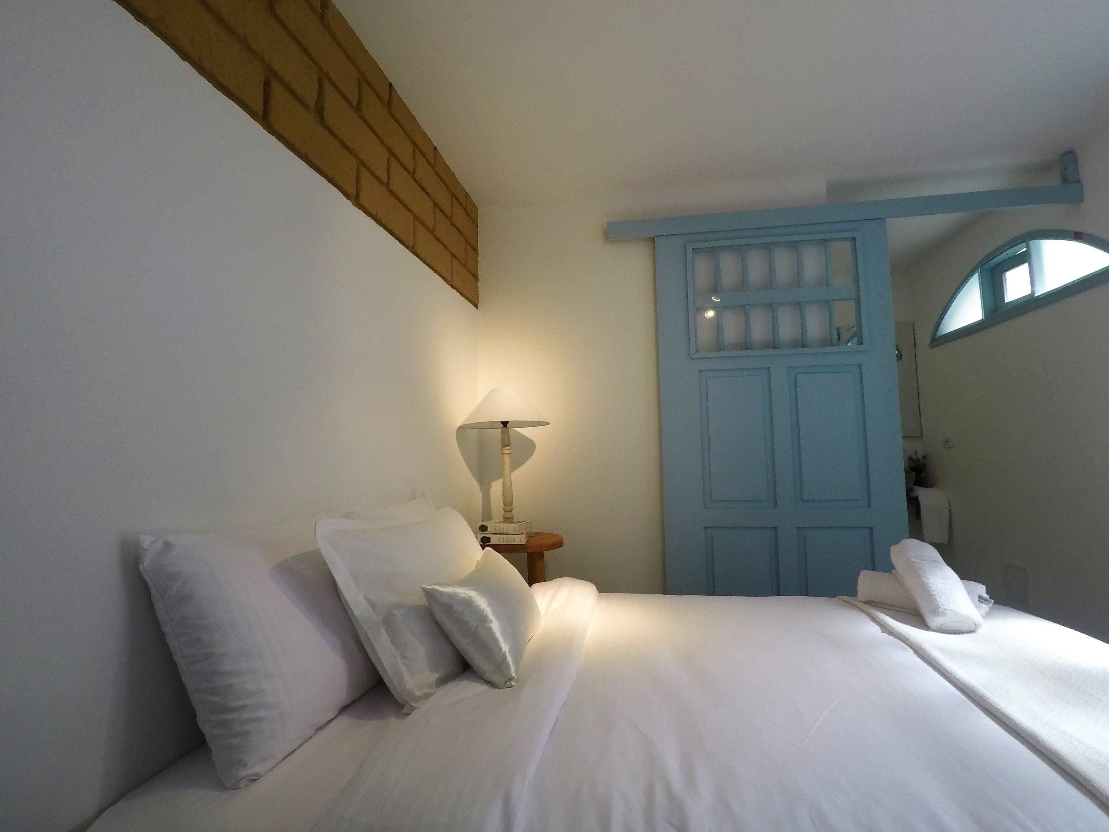 A neatly made bed with white linens and pillows, a bedside lamp, and a blue door with a window.