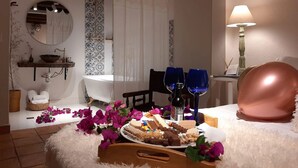 A cozy room with a wooden bed, a round mirror, a small shelf with toiletries, a table with a plate of food and drinks, and a lamp. - Casa Boutique Villa de Leyva - Adults only (Villa de Leyva)