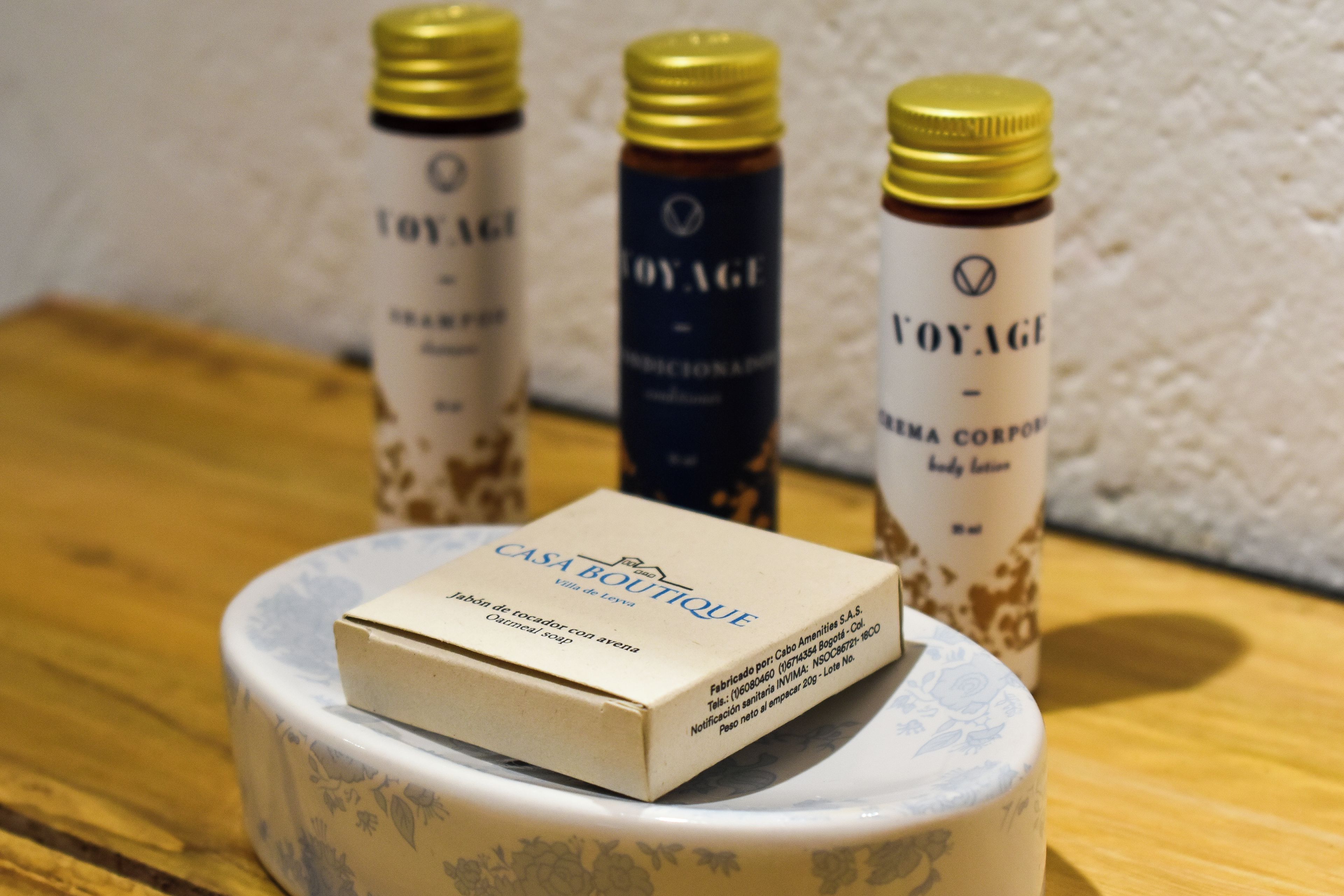Een doosje met de tekst 'CASA BOUTIQUE' op een decoratieve keramieken voet, met daarin het zichtbare 'VOYAGE' bodylotion in drie flessen.