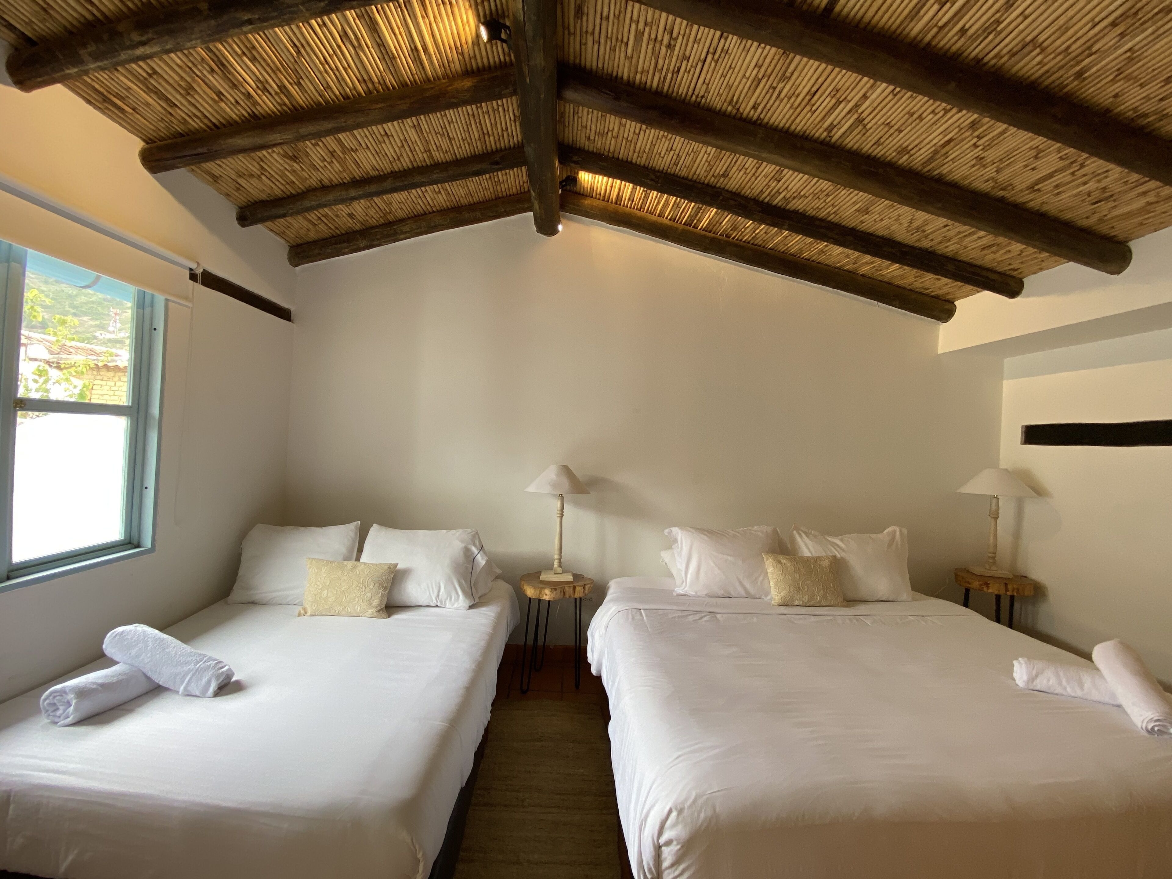 A hotel room with two beds, a wooden ceiling, and a window with a view.