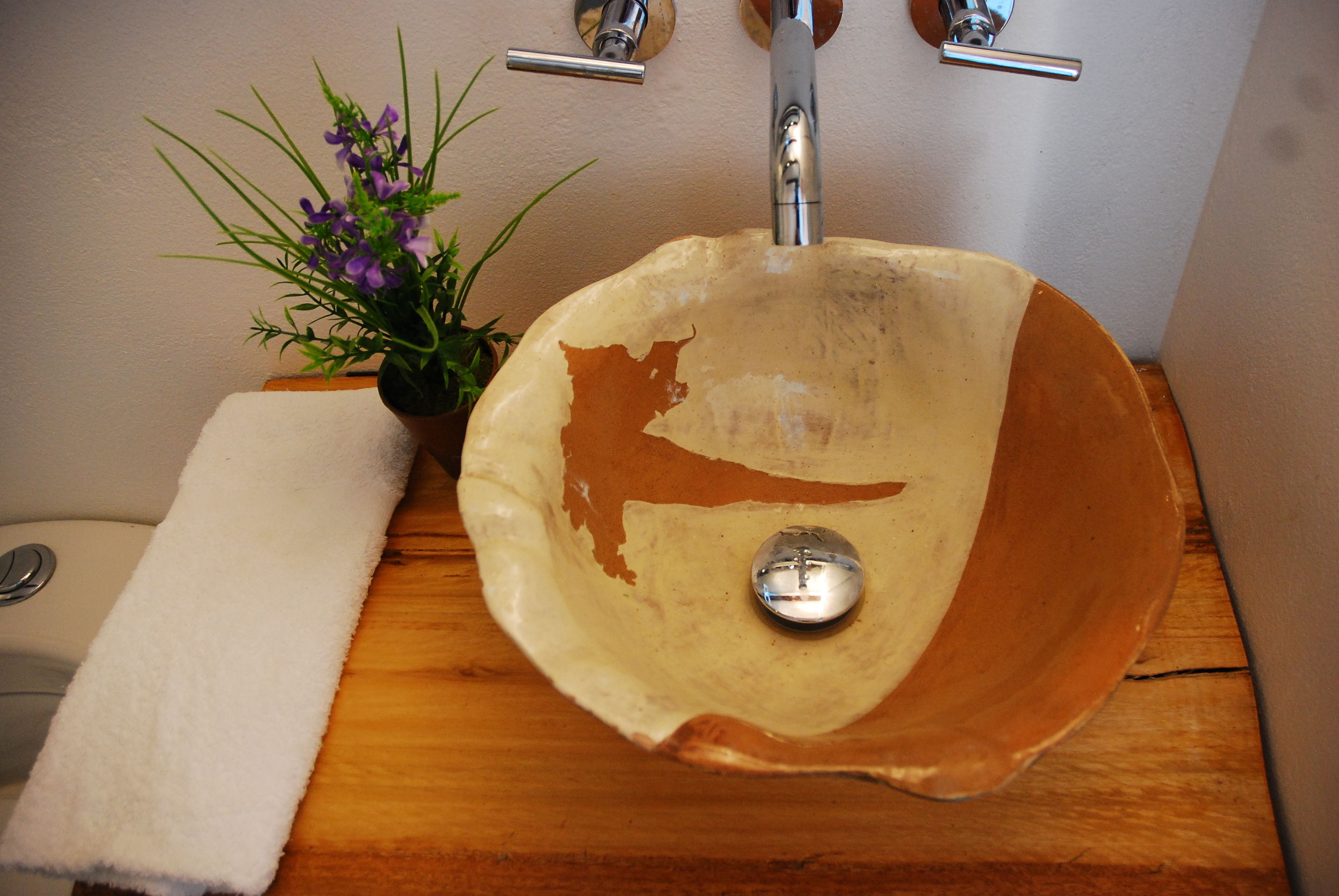 A bathroom sink with a unique bowl design, a faucet, and a small plant beside it.