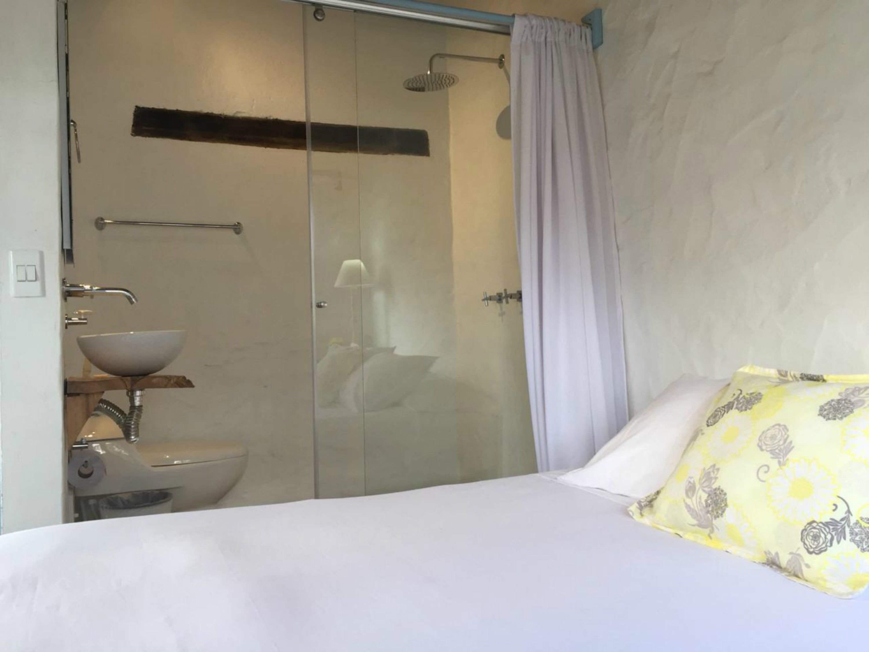A hotel room with a bed, a bathroom with a glass shower enclosure, a sink, and a toilet.