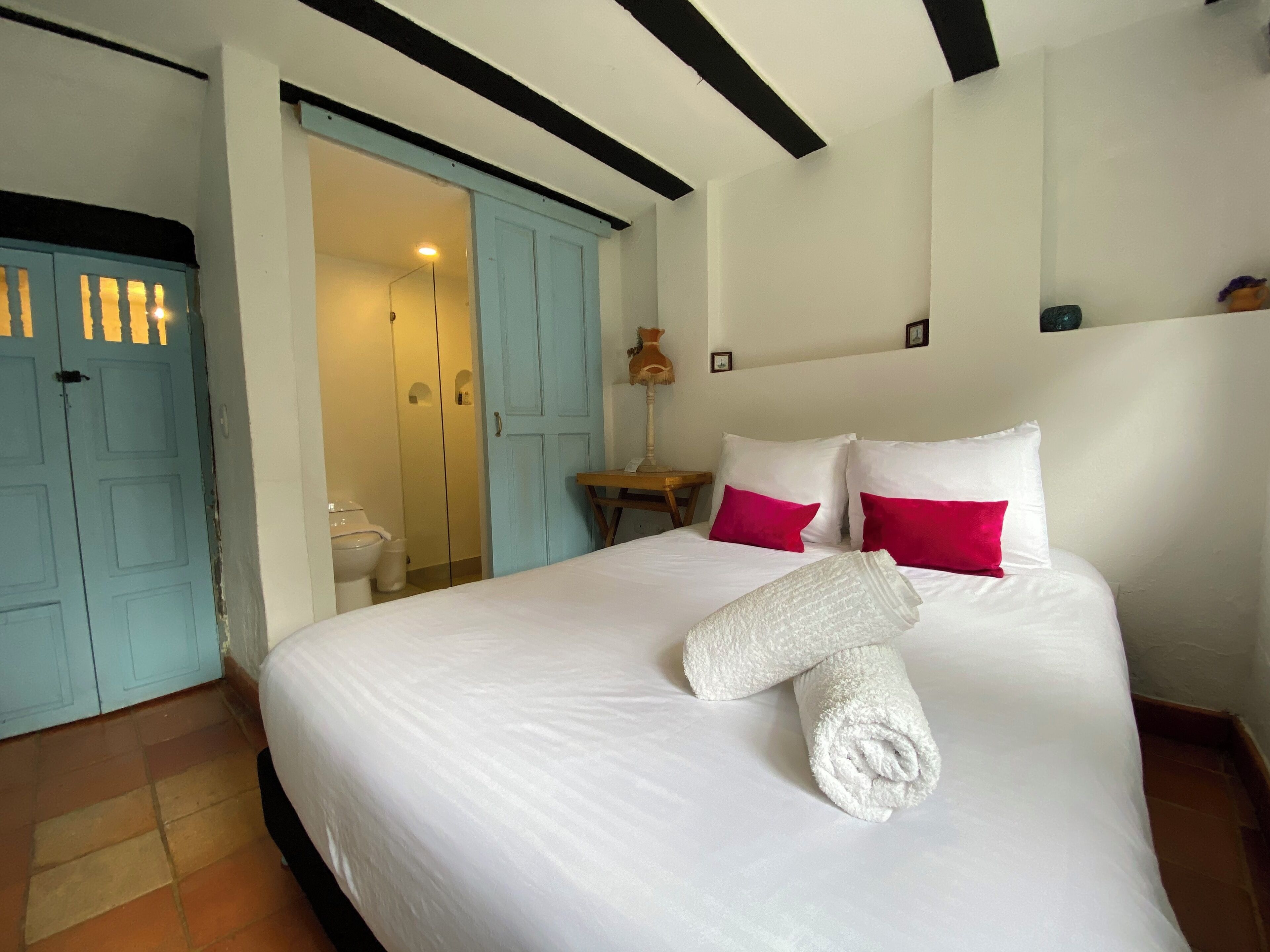 Une chambre d’hôtel avec un lit, du linge de lit blanc, une serviette roulée et une table de chevet avec une lampe.