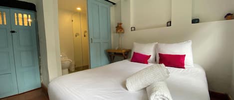 Une chambre d’hôtel avec un lit, du linge de lit blanc, une serviette roulée et une table de chevet avec une lampe.