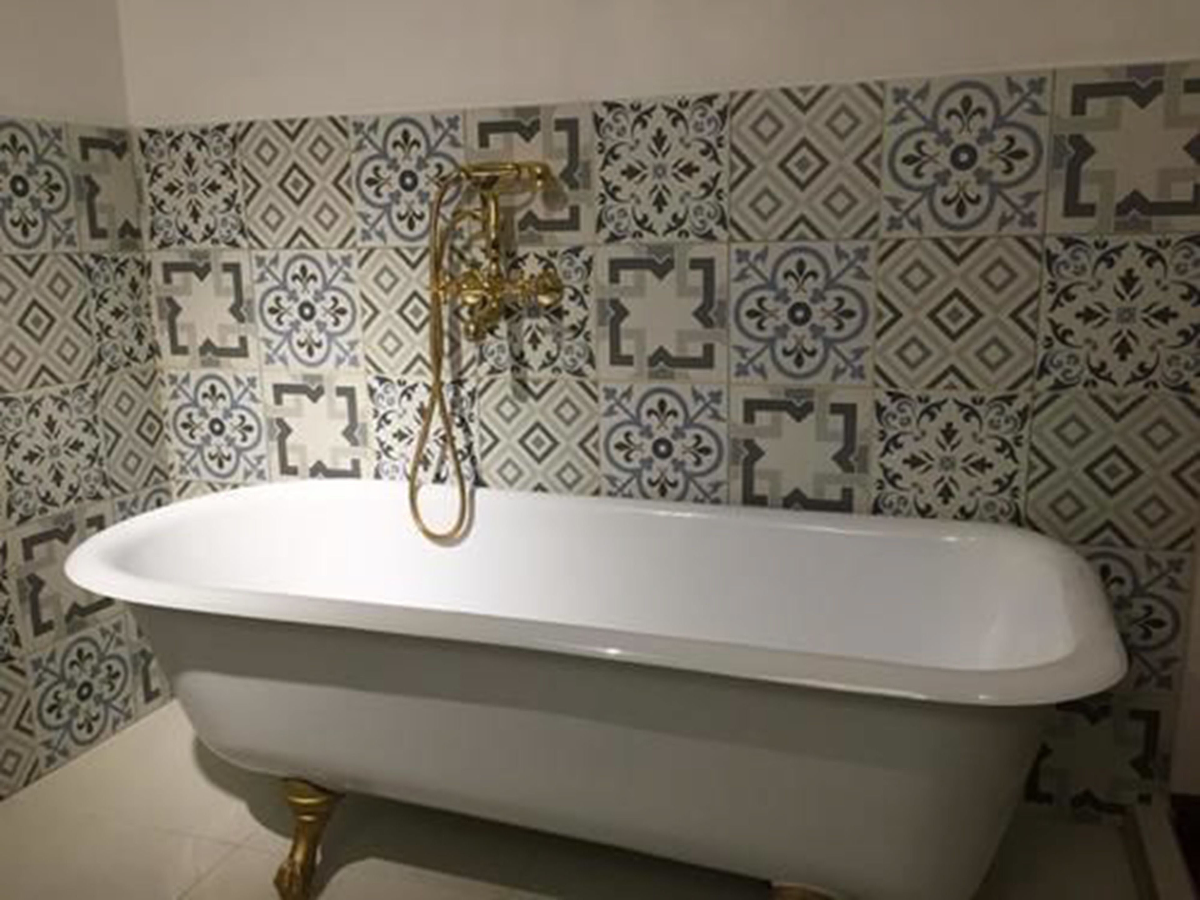 A bathroom with a freestanding bathtub, a gold showerhead, and patterned tiles on the walls.