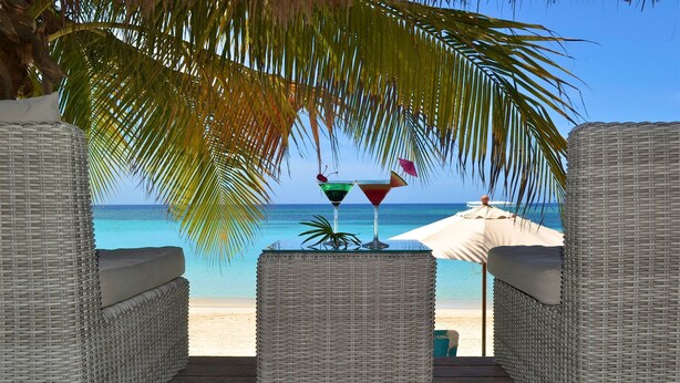 A beachside lounge with wicker furniture, two cocktails on a table, and a beach umbrella. - MAYAN PRINCESS BEACH AND DIVE RESORT (ROATAN)