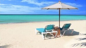 A beach with two lounge chairs and an umbrella. - MAYAN PRINCESS BEACH AND DIVE RESORT (ROATAN)