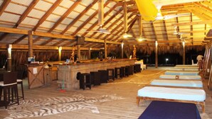 A spacious indoor area with a high ceiling, wooden beams, and a bar area with stools. There are several benches along the walls. - MAYAN PRINCESS BEACH AND DIVE RESORT (ROATAN)