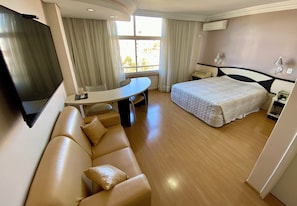 Ett hotellrum med en säng, en soffa, ett skrivbord, en tv och ett fönster med gardiner.