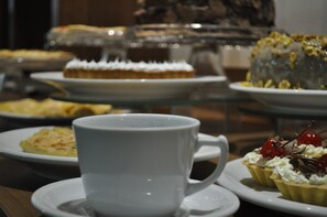 A dessert display with various cakes and pastries on a glass stand. - Hotel Maerkli (Santo Angelo)