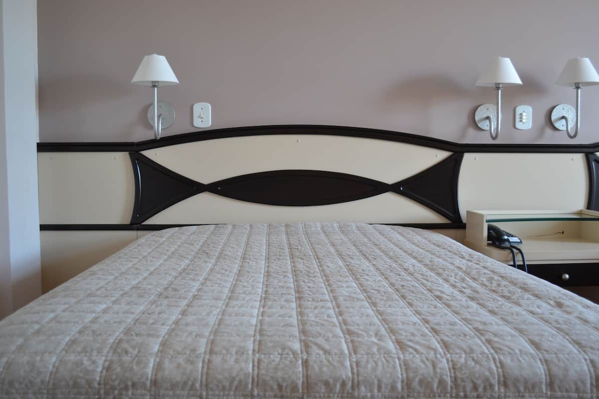 Ein Bett mit gestepptem Kopfteil, Nachttischlampen, einem Nachttisch und einer Wandsteckdose.