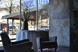 A hotel interior with a marble wall, a table with a white tablecloth, and two upholstered chairs. - Hotel Maerkli (Santo Angelo)