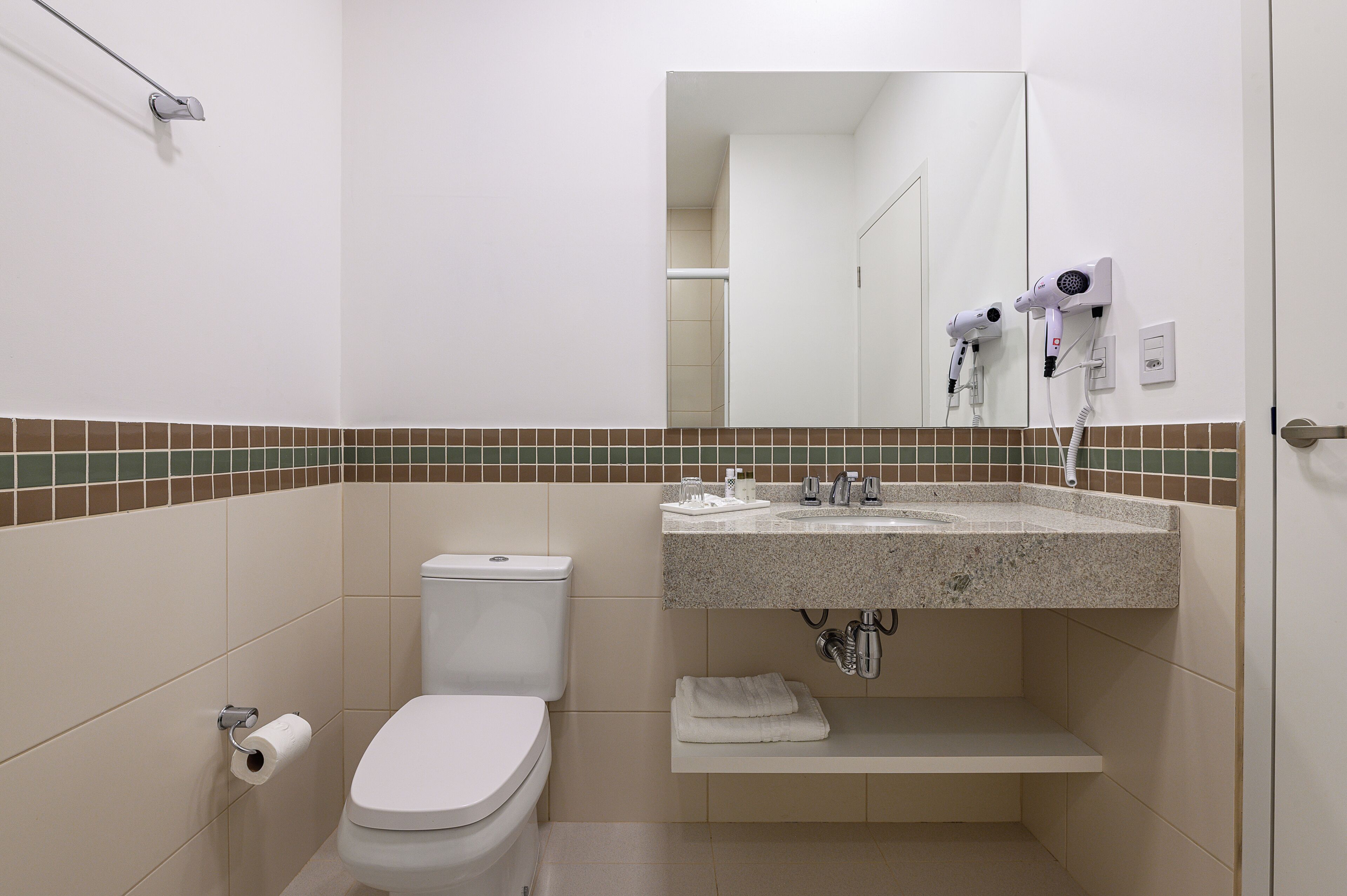 A bathroom with a toilet, sink, and hair dryer mounted on the wall.