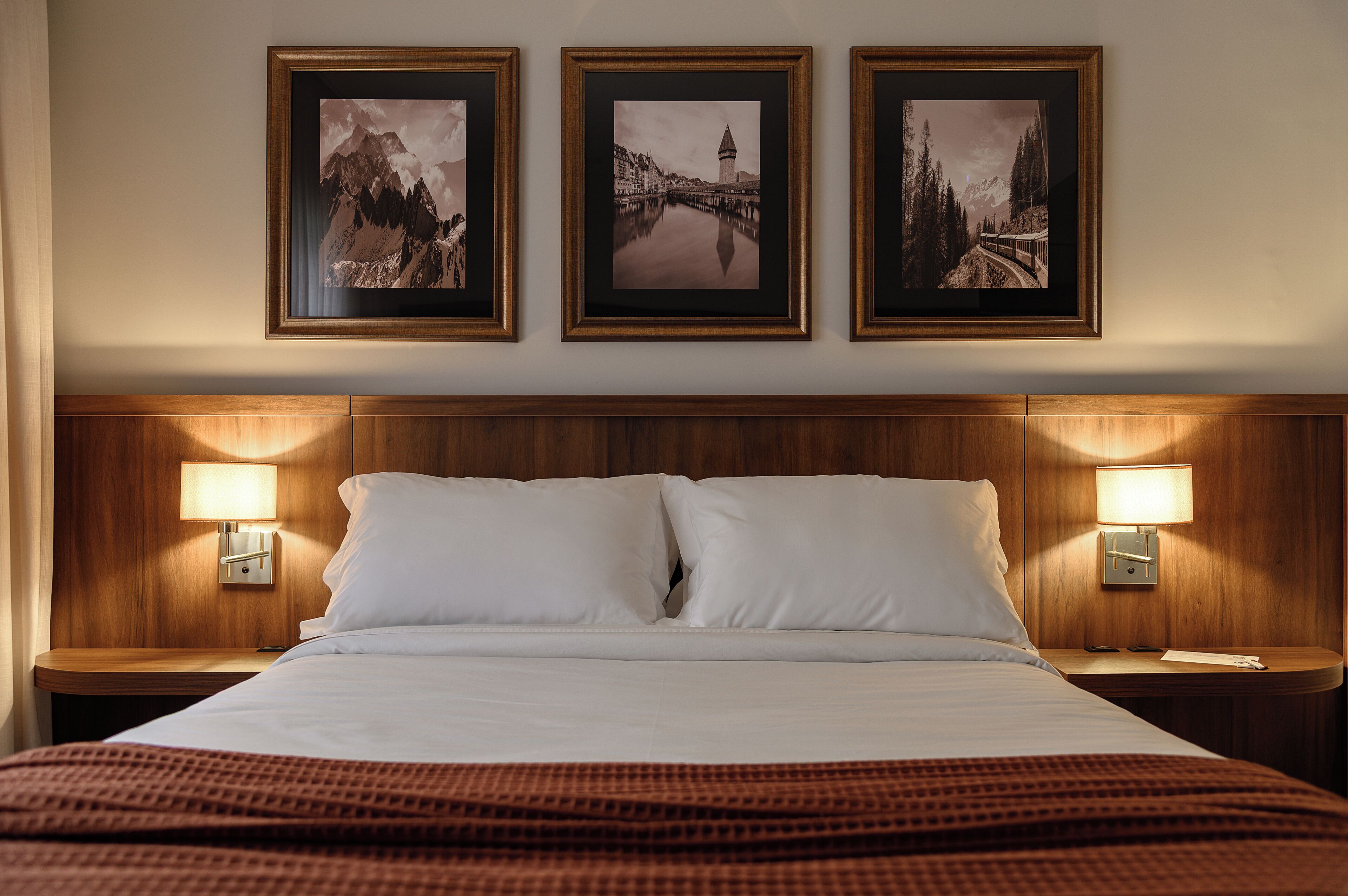 Habitación de hotel con una cama grande, dos lámparas de noche y tres cuadros en la pared.