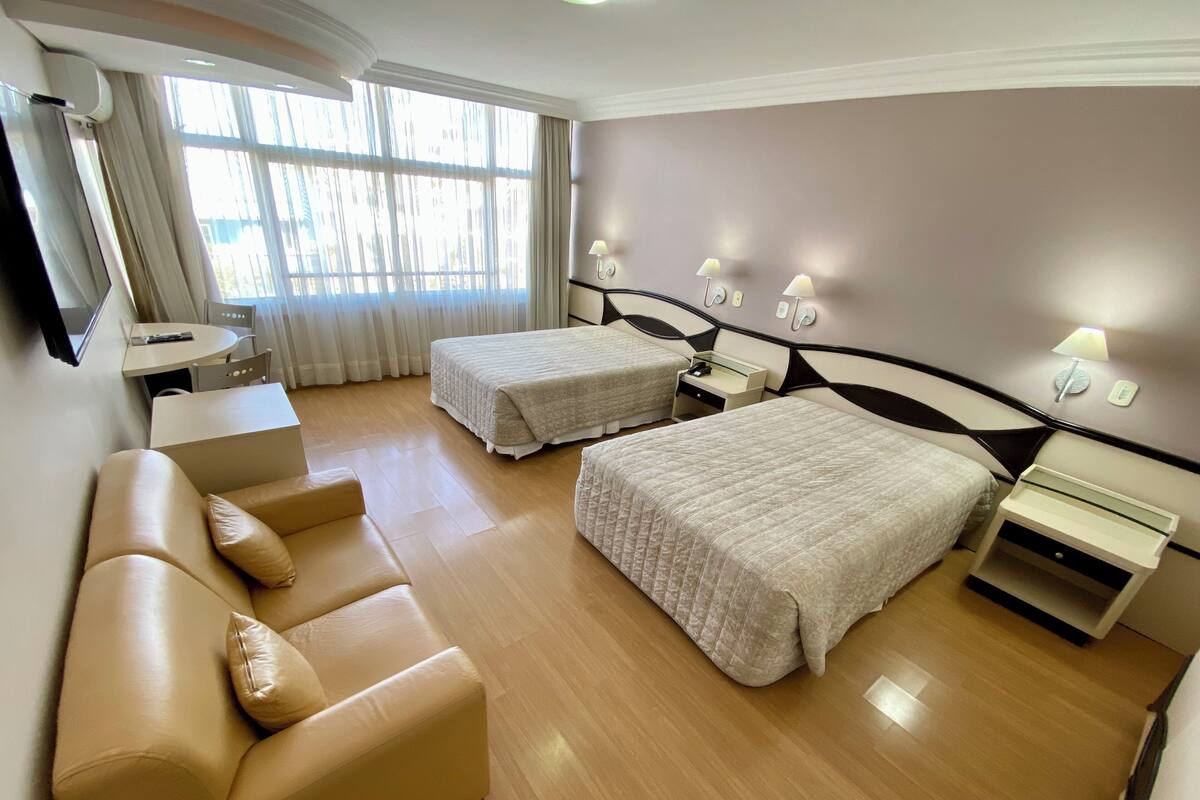 Ein Hotelzimmer mit zwei Betten, einer Couch, einem Schreibtisch und einem Fenster mit Vorhängen.