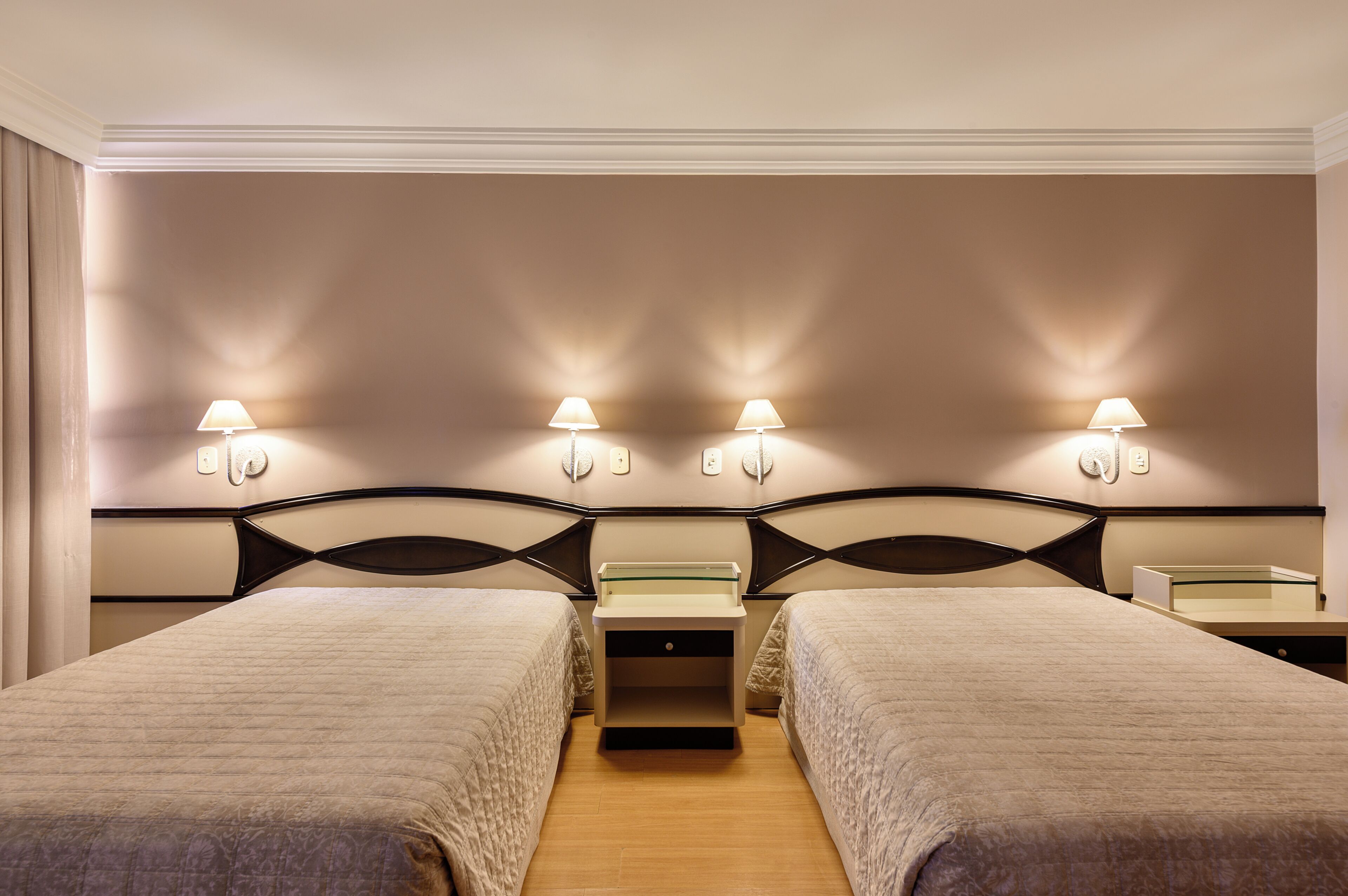 Une chambre d’hôtel avec deux lits, une table de chevet et des lampes fixées au mur.