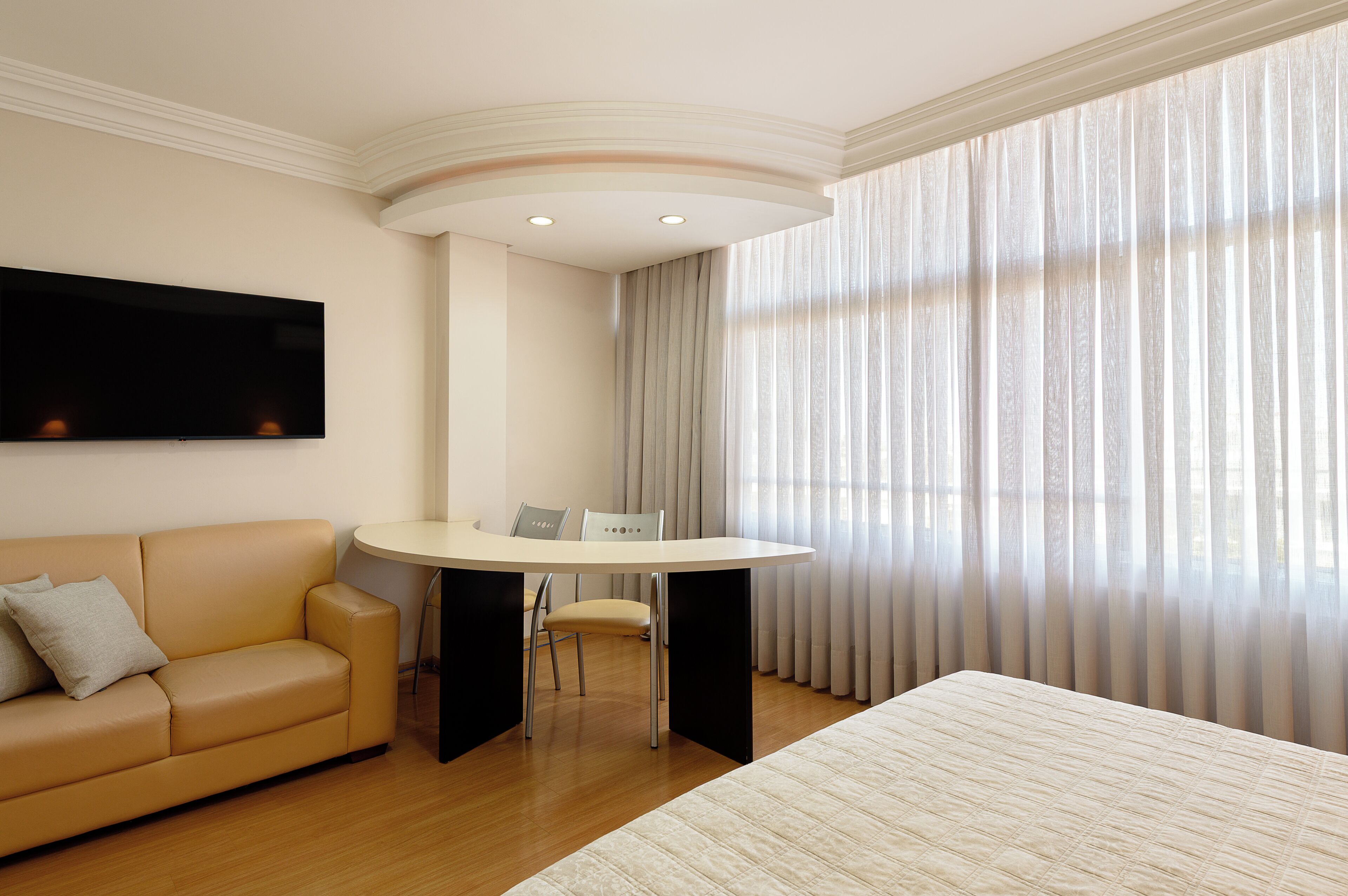 A hotel room with a bed, a sofa, a dining table, and a TV.