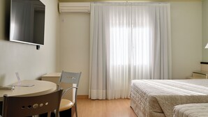 A hotel room with a bed, a desk with a chair, a television, and a window with curtains. - Hotel Maerkli (Santo Angelo)