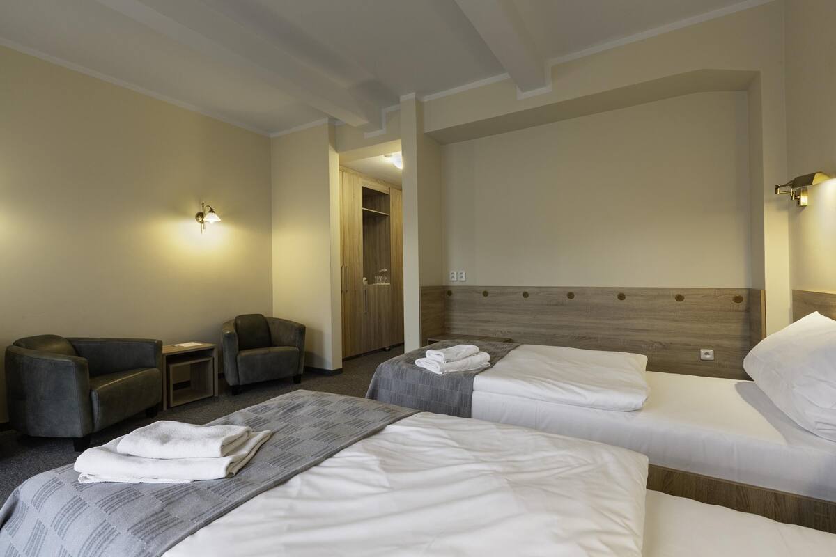 A hotel room with two beds, a sofa, a chair, and a wooden wardrobe.