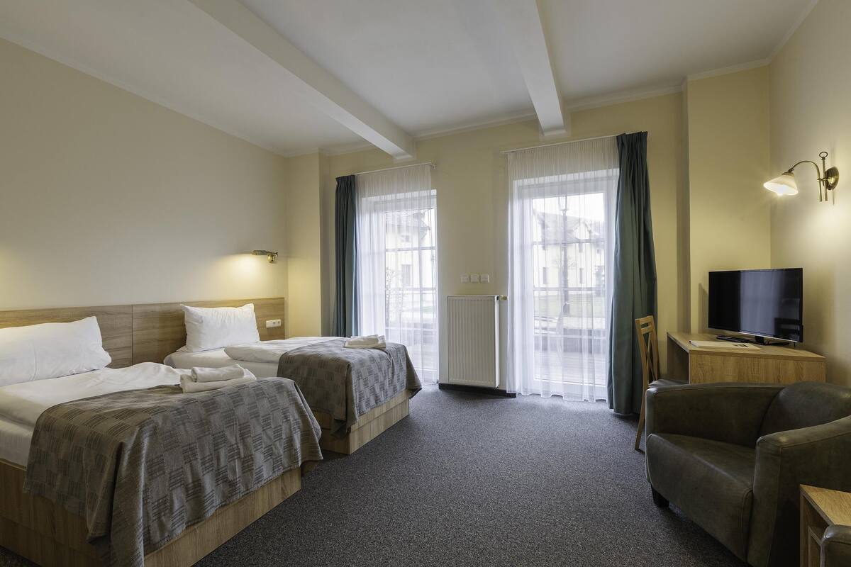 A hotel room with two beds, a TV, a chair, and a desk.