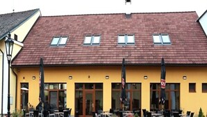 A yellow building with a red-tiled roof, outdoor seating, and a garden area. - Statek 1738 (Vsestudy)