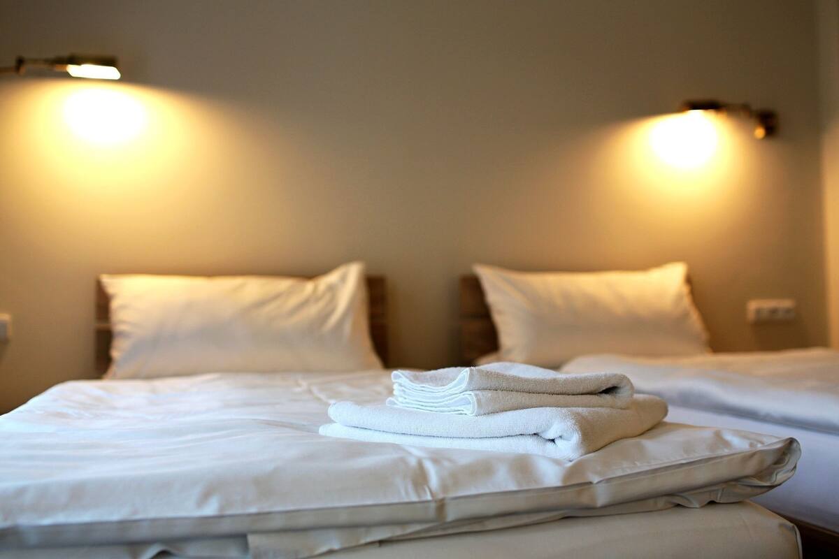A hotel room with two beds, each with white linens and pillows, and two wall-mounted lights.